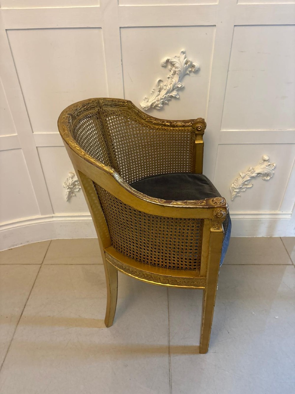 A pair of French Louis XVI style carved giltwood tub armchairs featuring curved caned backs and dark blue velvet seat cushions. View IX