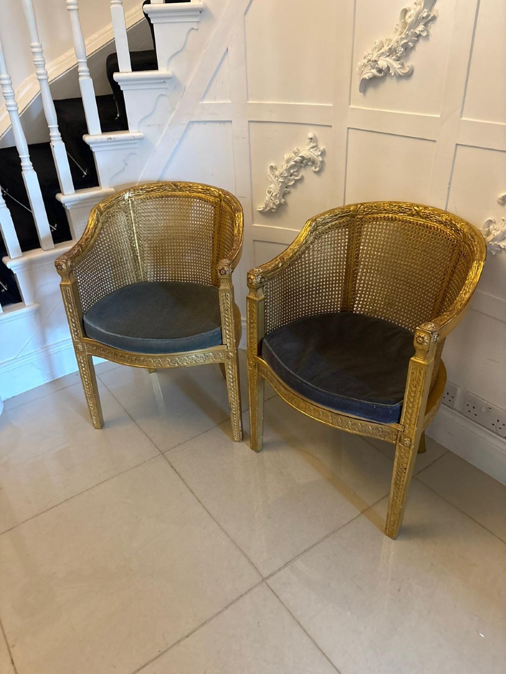 A pair of French Louis XVI style carved giltwood tub armchairs featuring curved caned backs and dark blue velvet seat cushions. View XIV