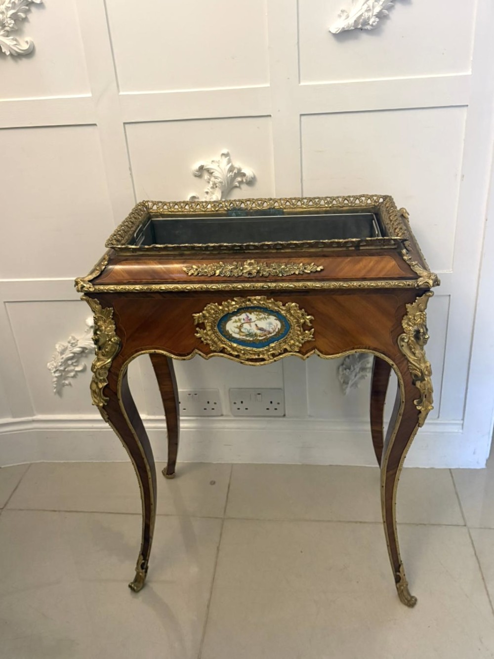 A Louis XV style kingwood jardiniere stand with ornate gilt-bronze ormolu mounts, cabriole legs, and a central porcelain plaque.