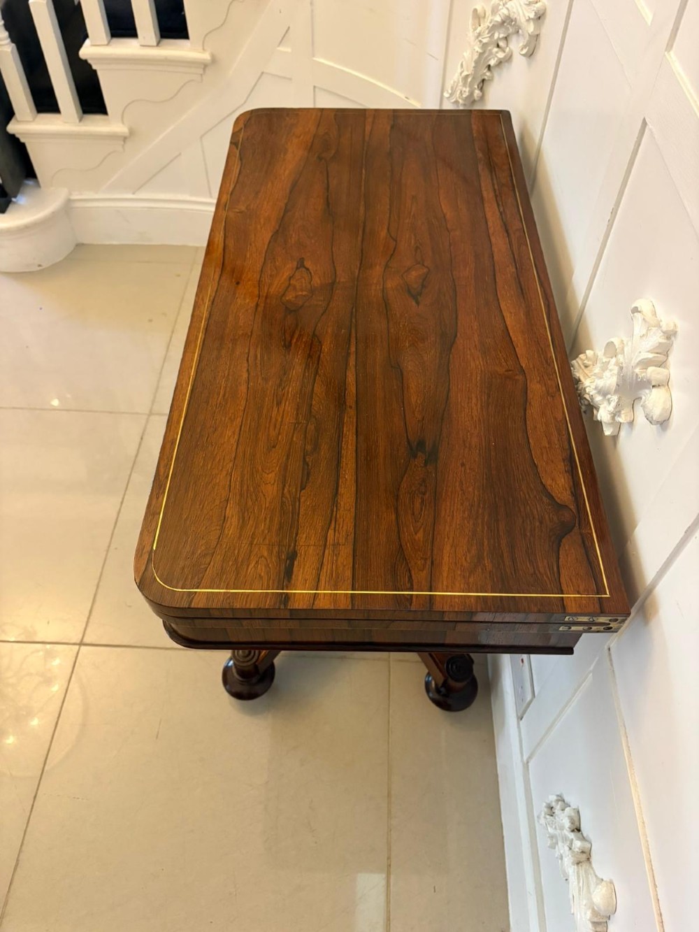A Regency rosewood card table featuring fine brass inlay stringing, a fold-over swivel top, a central pedestal stem, and a quadform base on round feet. View V