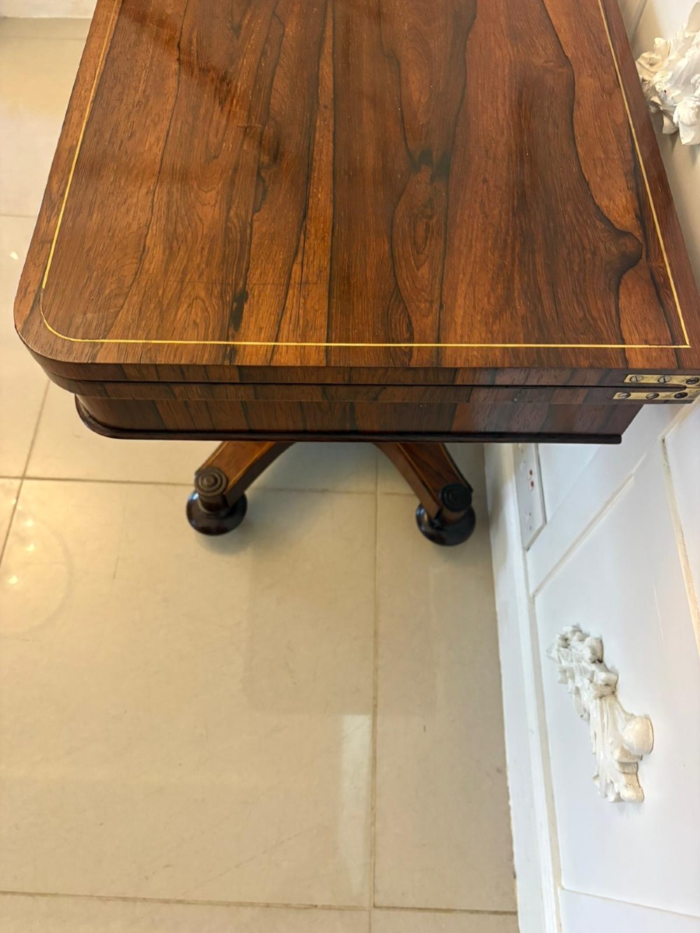 A Regency rosewood card table featuring fine brass inlay stringing, a fold-over swivel top, a central pedestal stem, and a quadform base on round feet. View VI