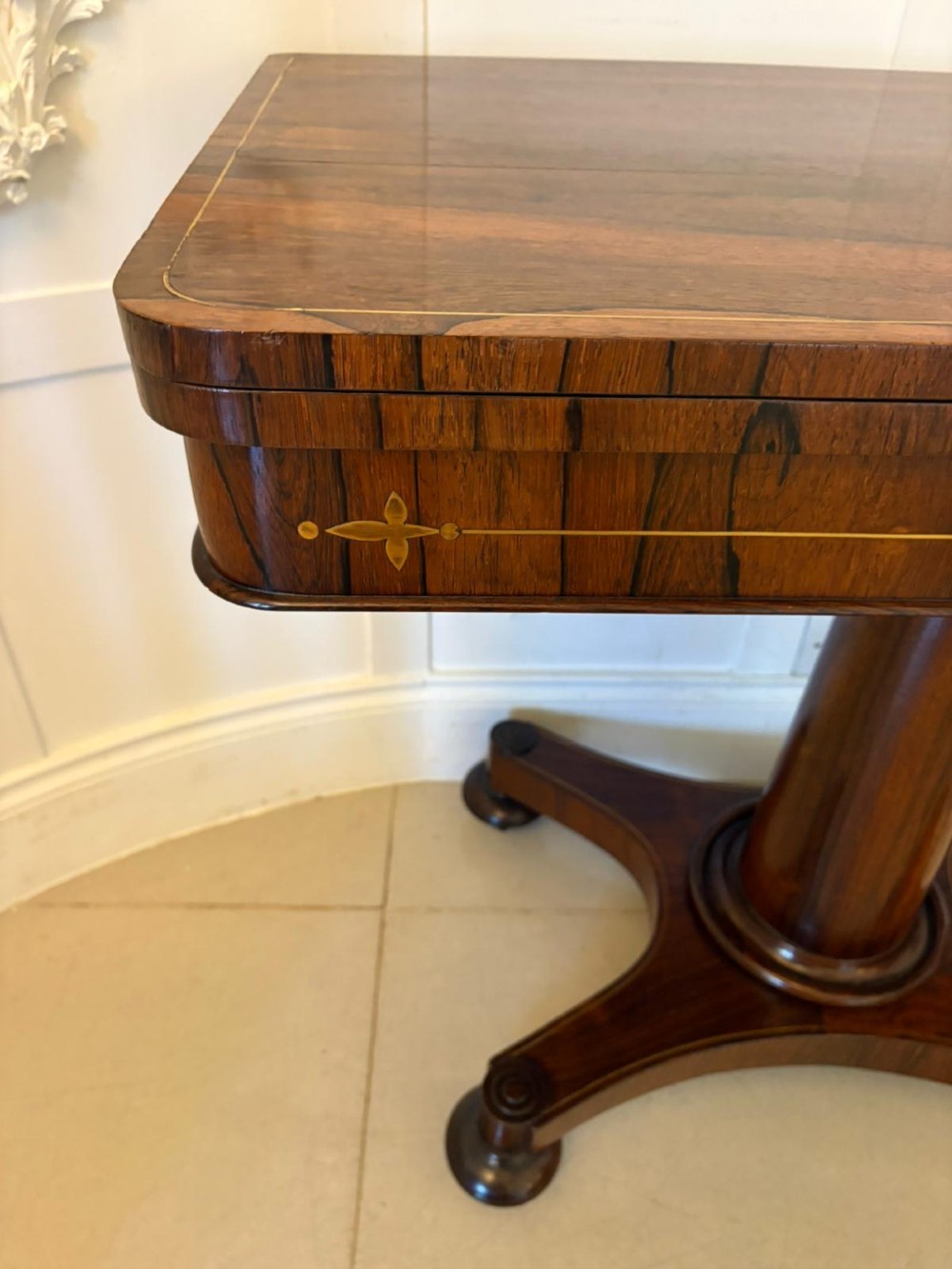 A Regency rosewood card table featuring fine brass inlay stringing, a fold-over swivel top, a central pedestal stem, and a quadform base on round feet. View IX