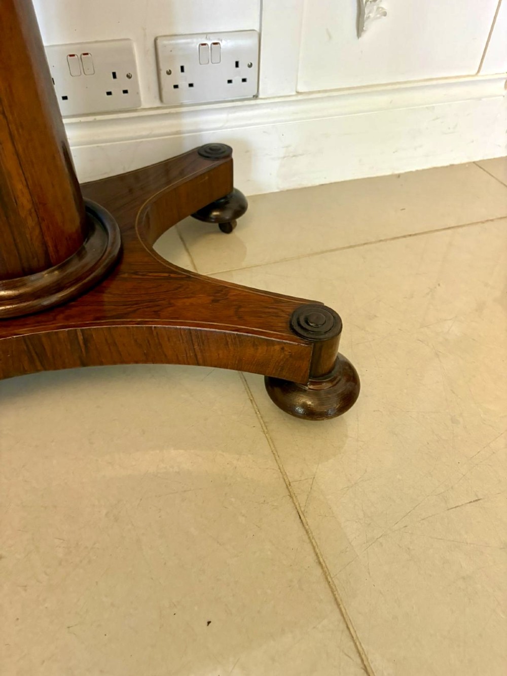A Regency rosewood card table featuring fine brass inlay stringing, a fold-over swivel top, a central pedestal stem, and a quadform base on round feet. View X