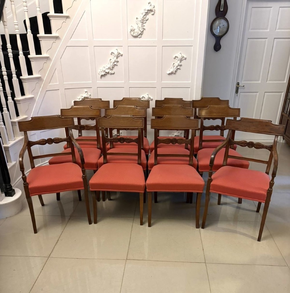 A set of twelve Regency mahogany dining chairs with carved mid-rails and coral fabric upholstered seats, including two matching carver armchairs.