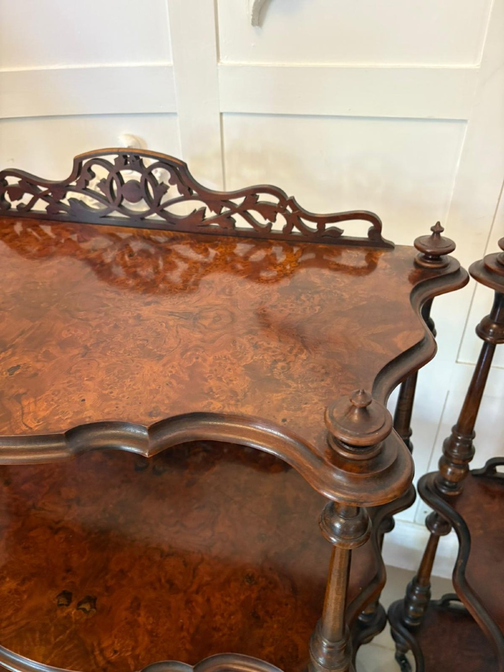 A pair of Victorian three-tier burr walnut whatnots featuring serpentine shelves, fretwork crestings, and turned support columns on castors. View VII