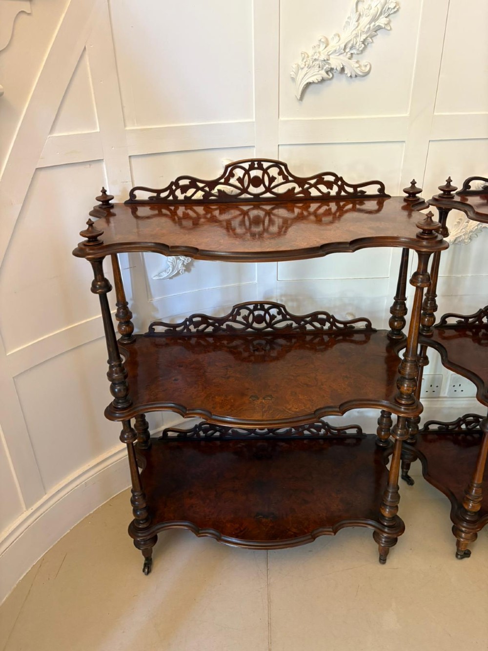 A pair of Victorian three-tier burr walnut whatnots featuring serpentine shelves, fretwork crestings, and turned support columns on castors. View IX