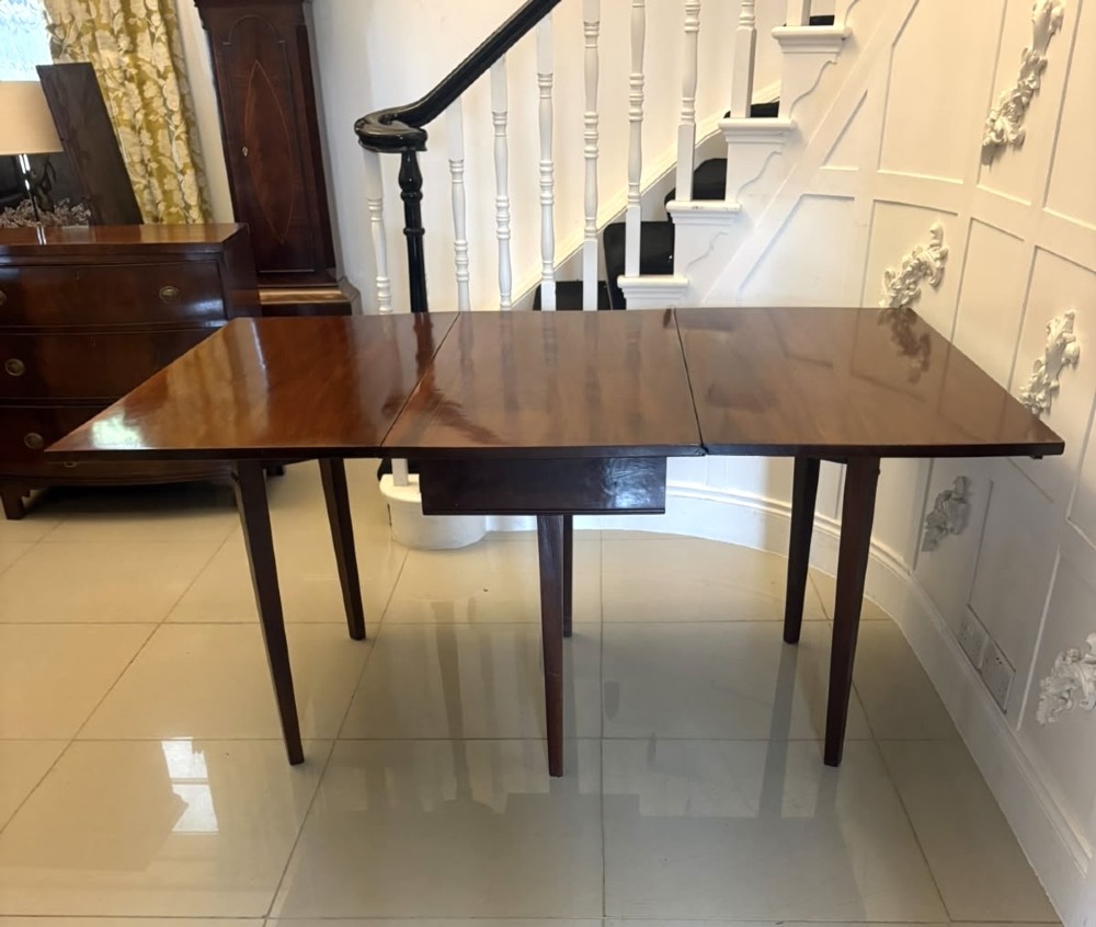 An antique Georgian mahogany drop-leaf dining table shown folded closed with square straight legs and a polished dark wood surface. View VII