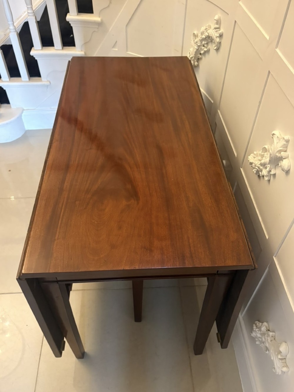 An antique Georgian mahogany drop-leaf dining table shown folded closed with square straight legs and a polished dark wood surface. View XI