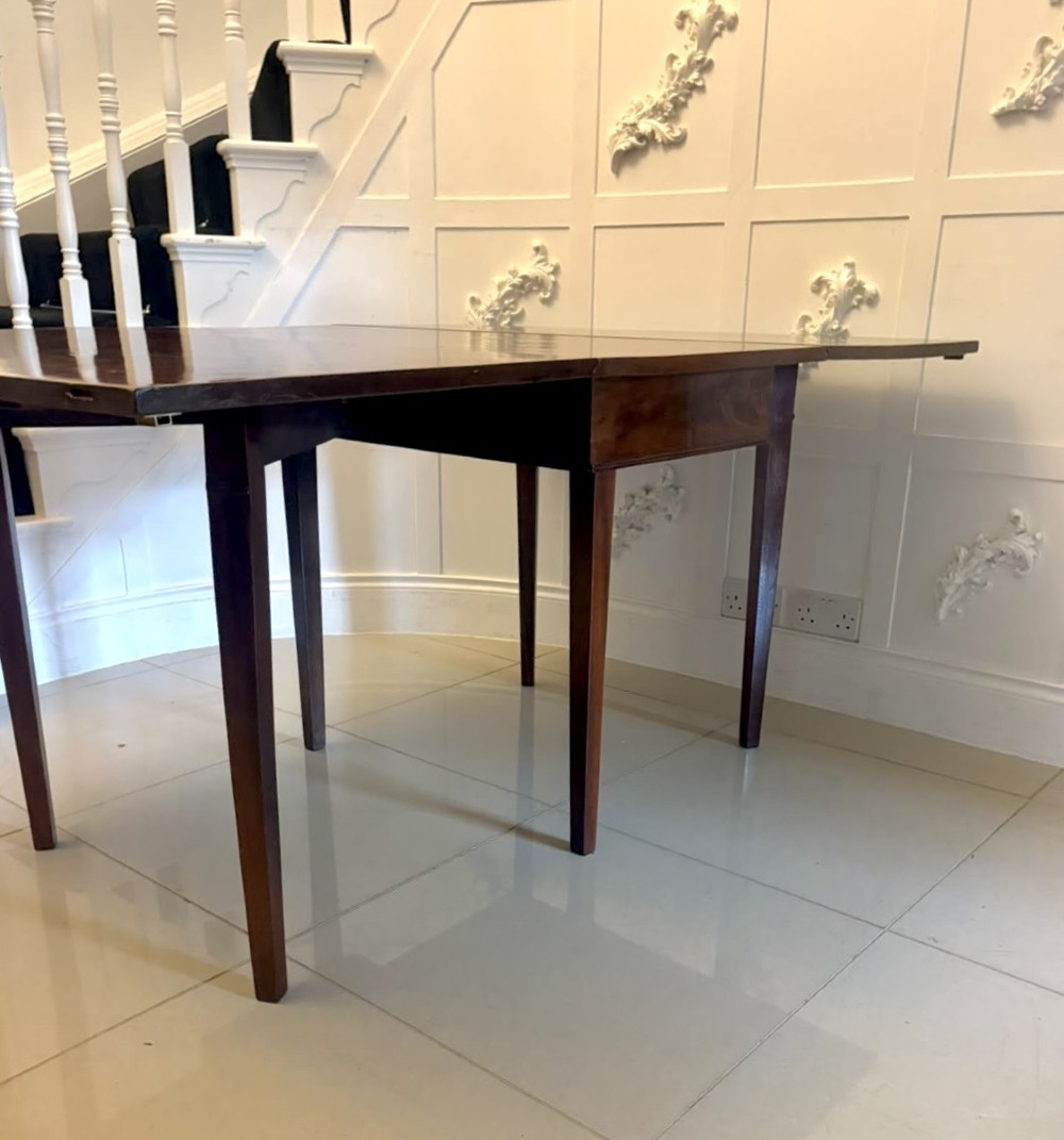 An antique Georgian mahogany drop-leaf dining table shown folded closed with square straight legs and a polished dark wood surface. View XII