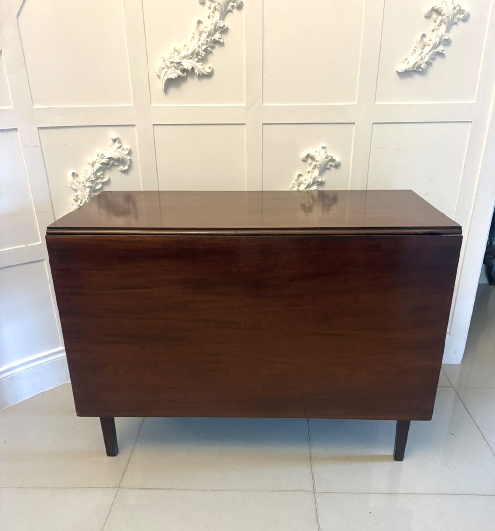 An antique Georgian mahogany drop-leaf dining table shown folded closed with square straight legs and a polished dark wood surface.