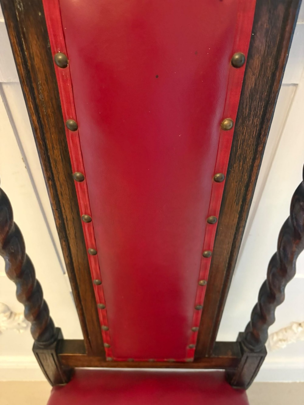 A set of high-backed dark oak dining chairs with barley twist uprights, carved cresting rails, and red upholstered seats and back panels with stud trim. View IV