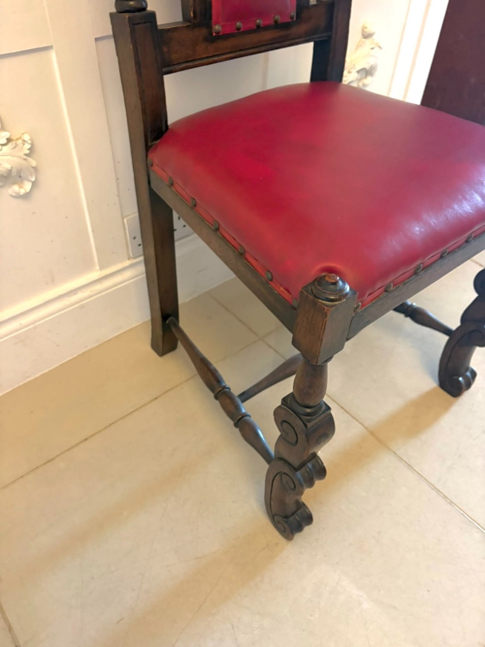 A set of high-backed dark oak dining chairs with barley twist uprights, carved cresting rails, and red upholstered seats and back panels with stud trim. View V