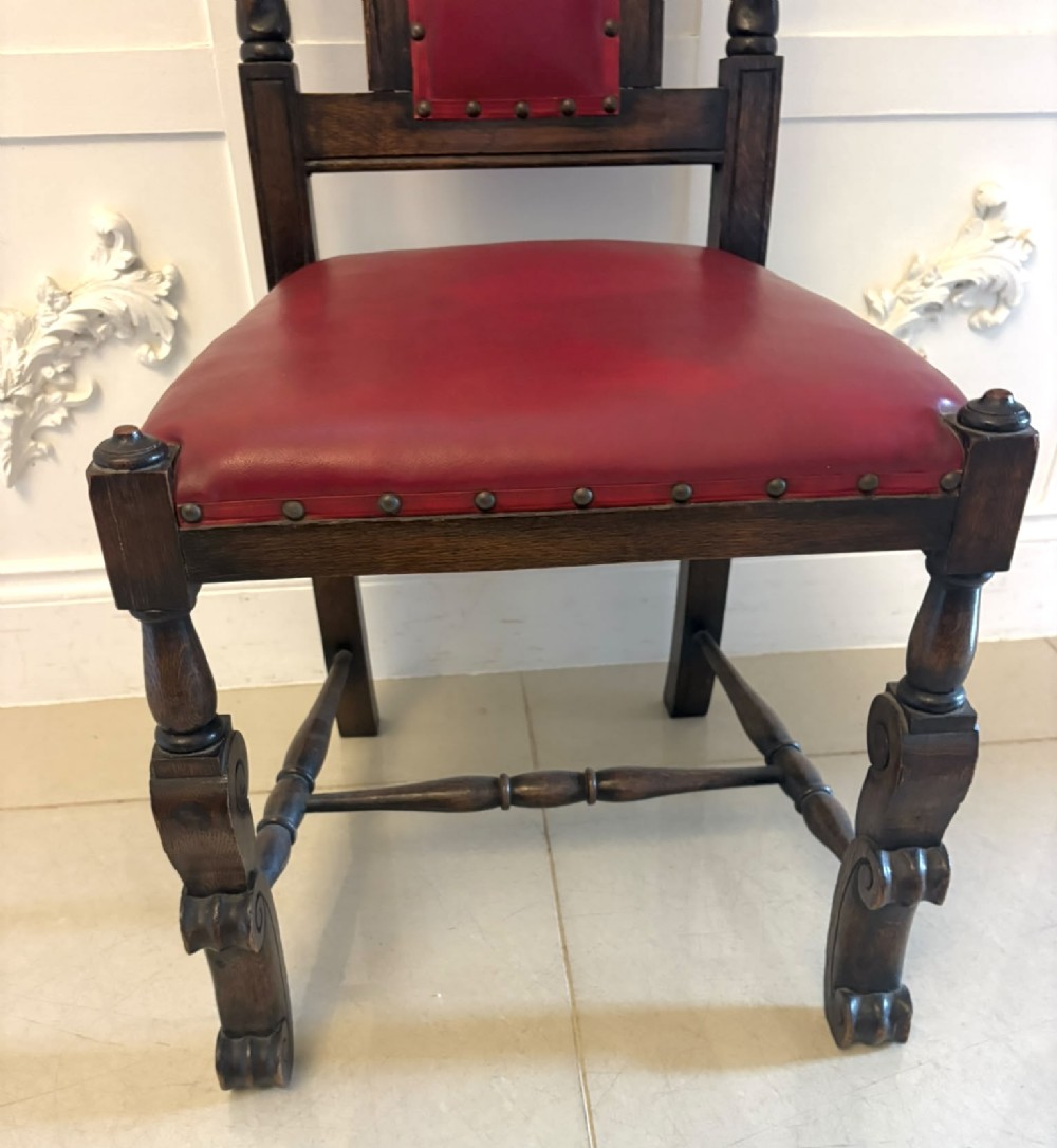 A set of high-backed dark oak dining chairs with barley twist uprights, carved cresting rails, and red upholstered seats and back panels with stud trim. View VI