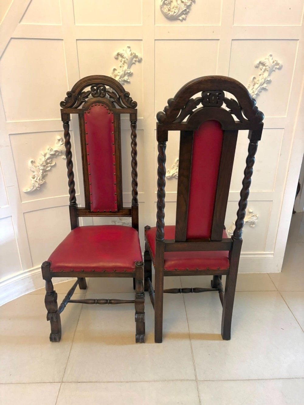 A set of high-backed dark oak dining chairs with barley twist uprights, carved cresting rails, and red upholstered seats and back panels with stud trim. View IX