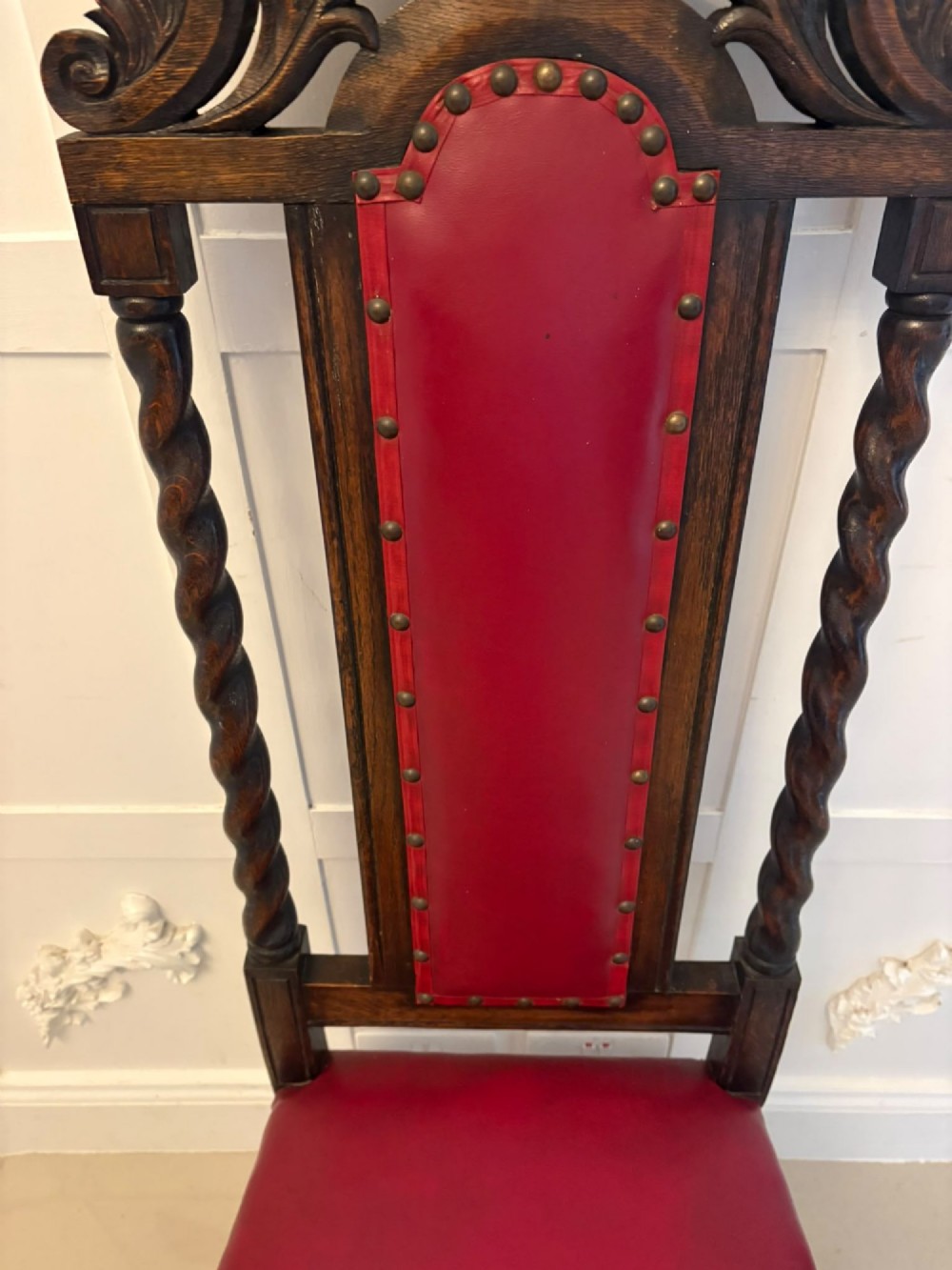A set of high-backed dark oak dining chairs with barley twist uprights, carved cresting rails, and red upholstered seats and back panels with stud trim. View XI