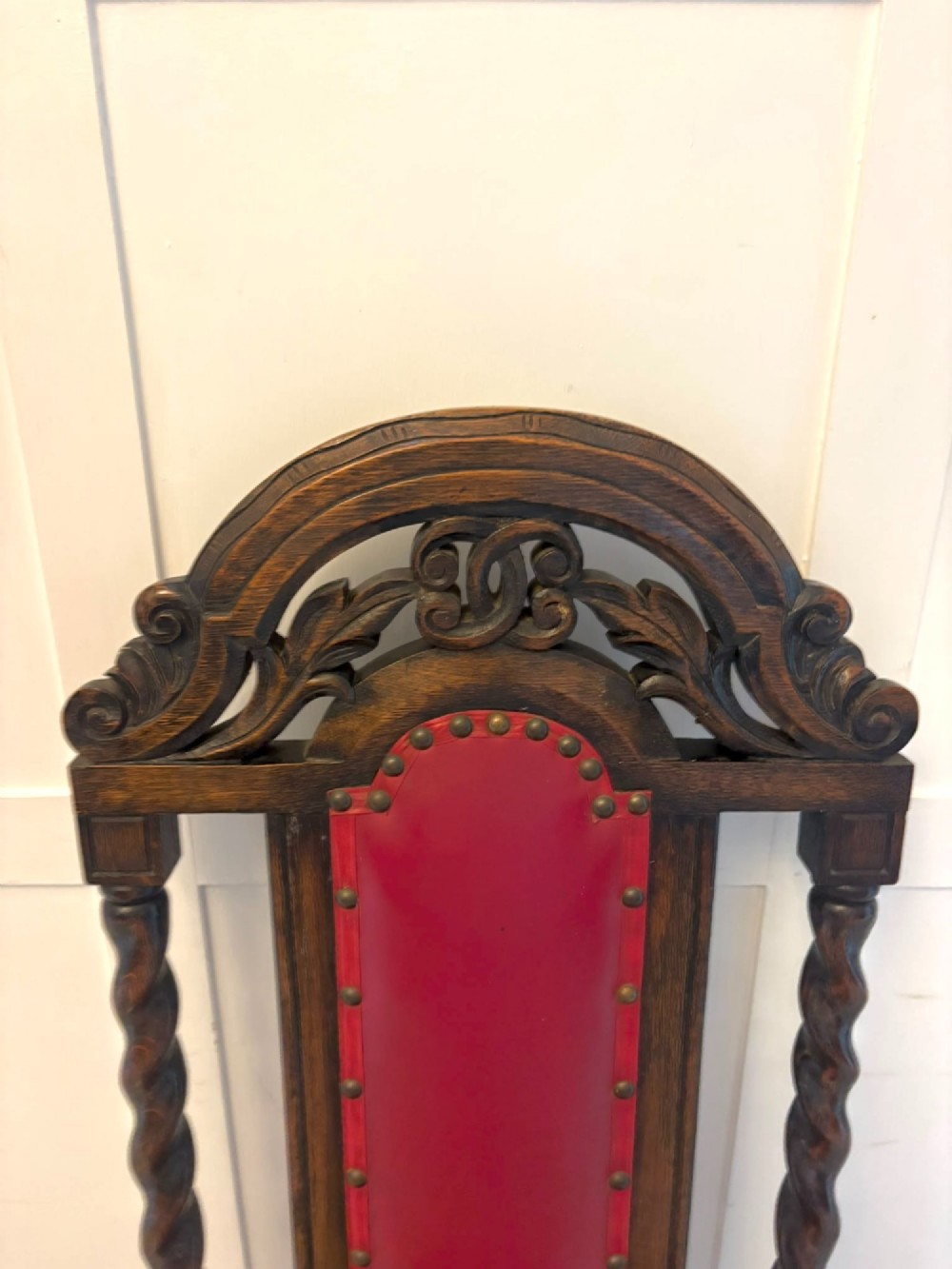 A set of high-backed dark oak dining chairs with barley twist uprights, carved cresting rails, and red upholstered seats and back panels with stud trim. View XII