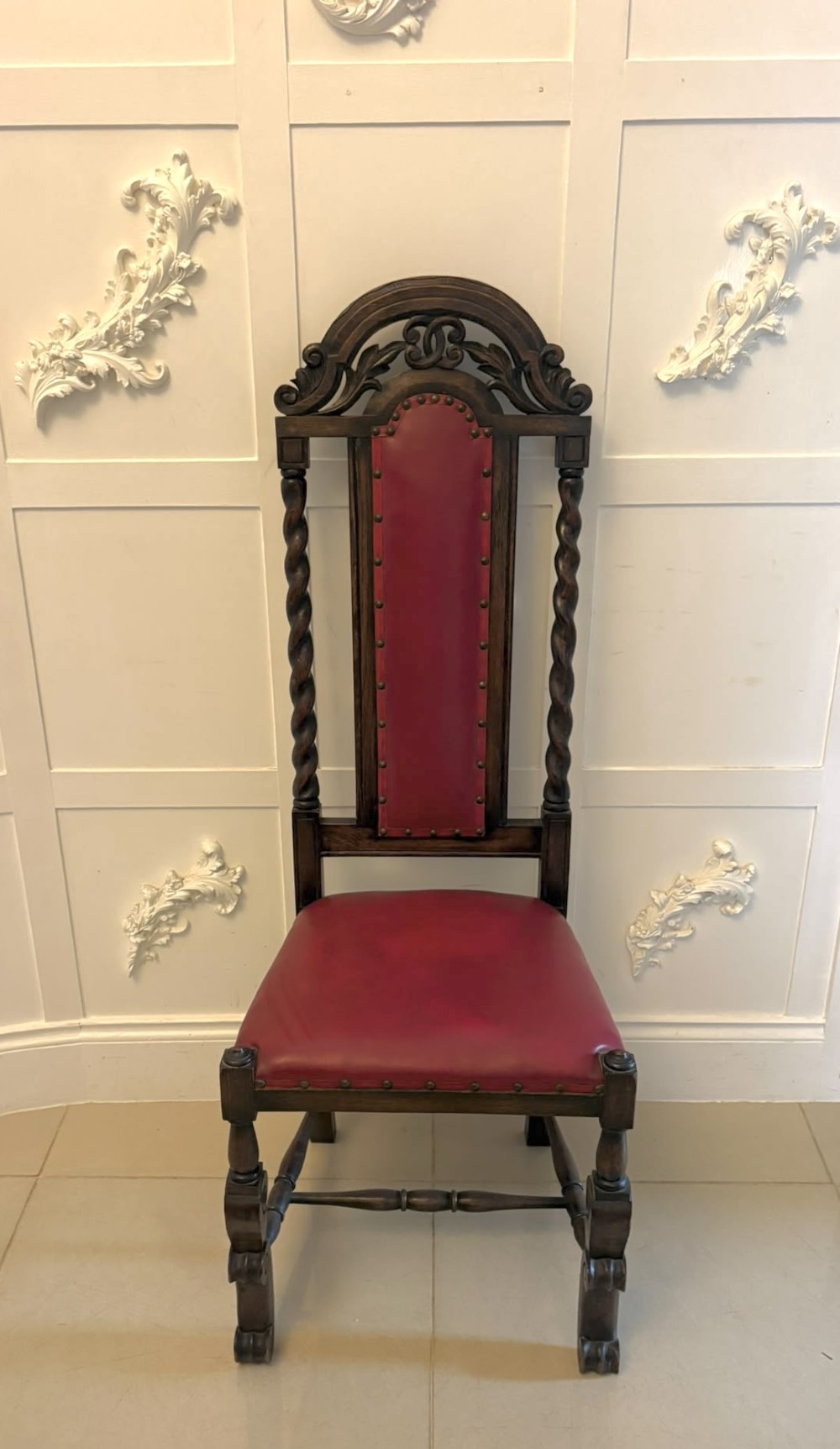 A set of high-backed dark oak dining chairs with barley twist uprights, carved cresting rails, and red upholstered seats and back panels with stud trim. View XIV