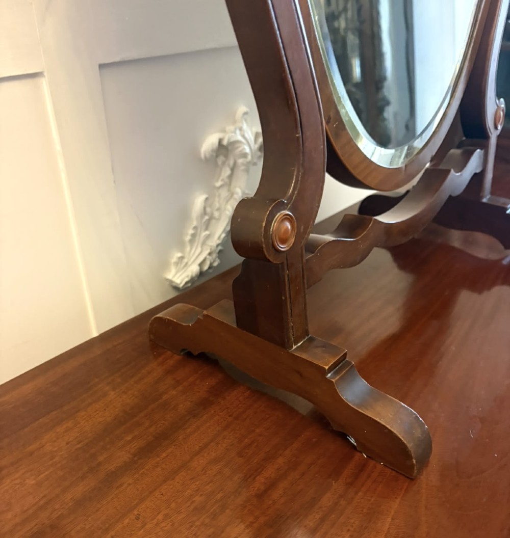 An Edwardian mahogany toilet mirror featuring a shield-shaped frame with bevelled glass mounted on a swivelling stand with brass knobs. View IV