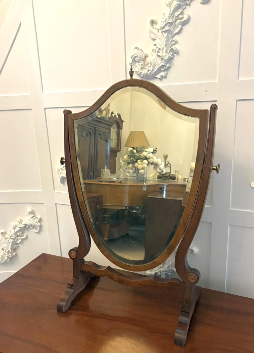 An Edwardian mahogany toilet mirror featuring a shield-shaped frame with bevelled glass mounted on a swivelling stand with brass knobs. View VIII