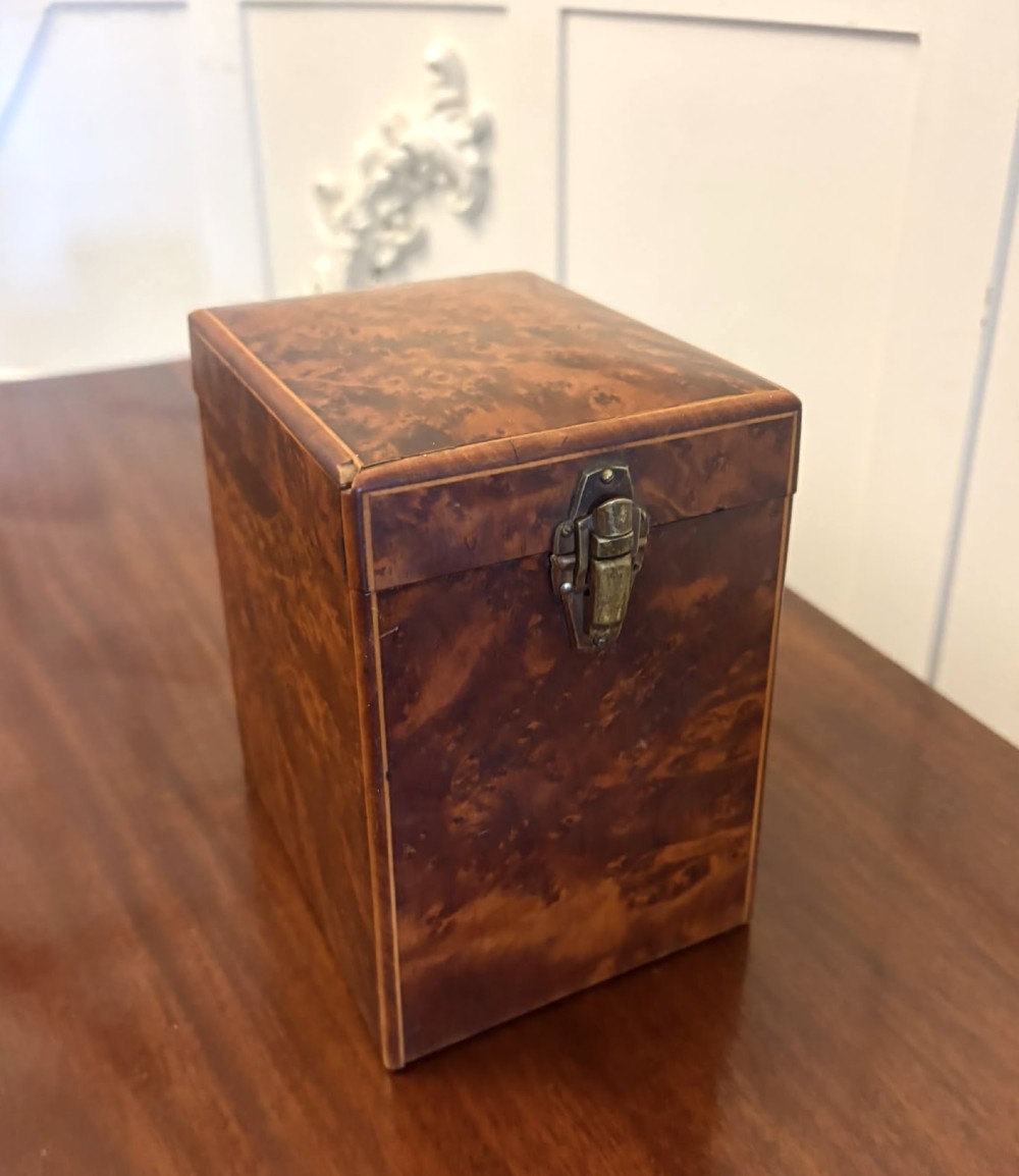 An upright Victorian travelling tea caddy crafted from amboyna burl wood with line inlay and a brass front latch.