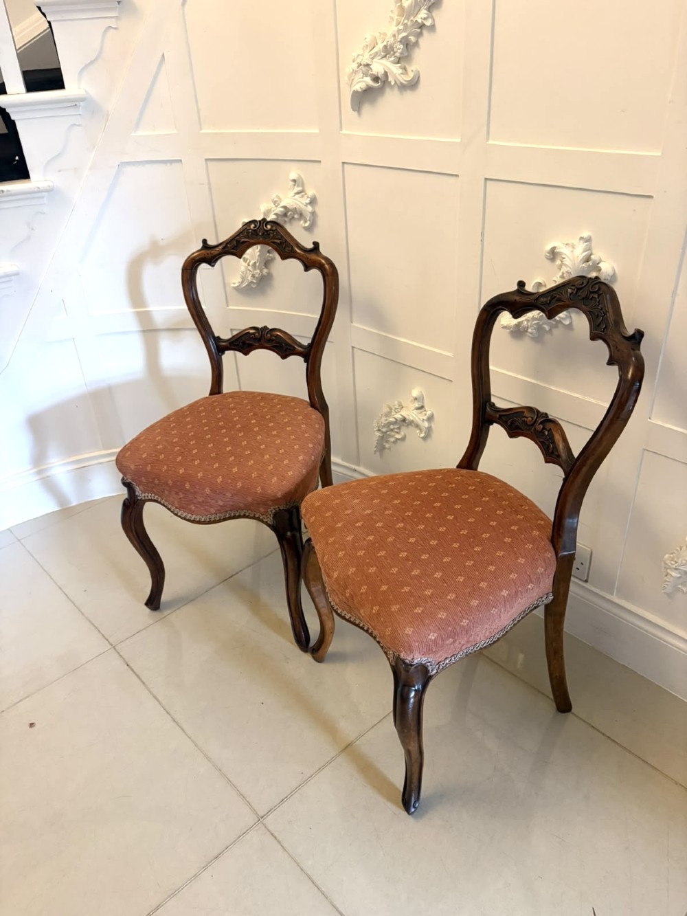 A pair of Victorian carved walnut side chairs featuring open balloon backs with foliate carvings, cabriole legs, and terracotta patterned fabric upholstered seats. View V