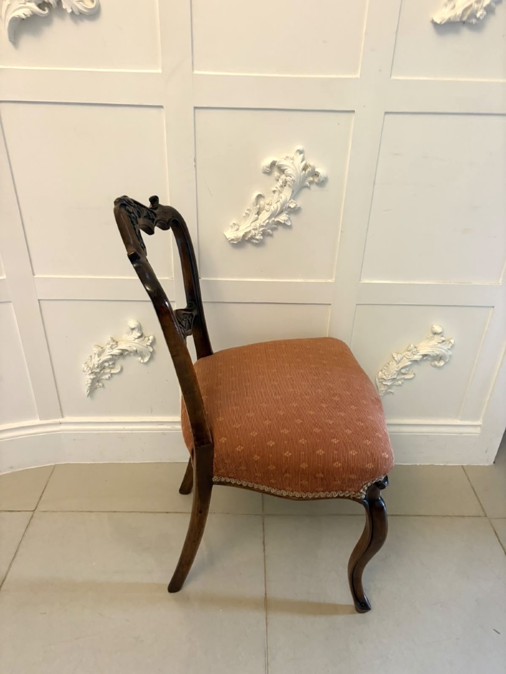 A pair of Victorian carved walnut side chairs featuring open balloon backs with foliate carvings, cabriole legs, and terracotta patterned fabric upholstered seats. View VI