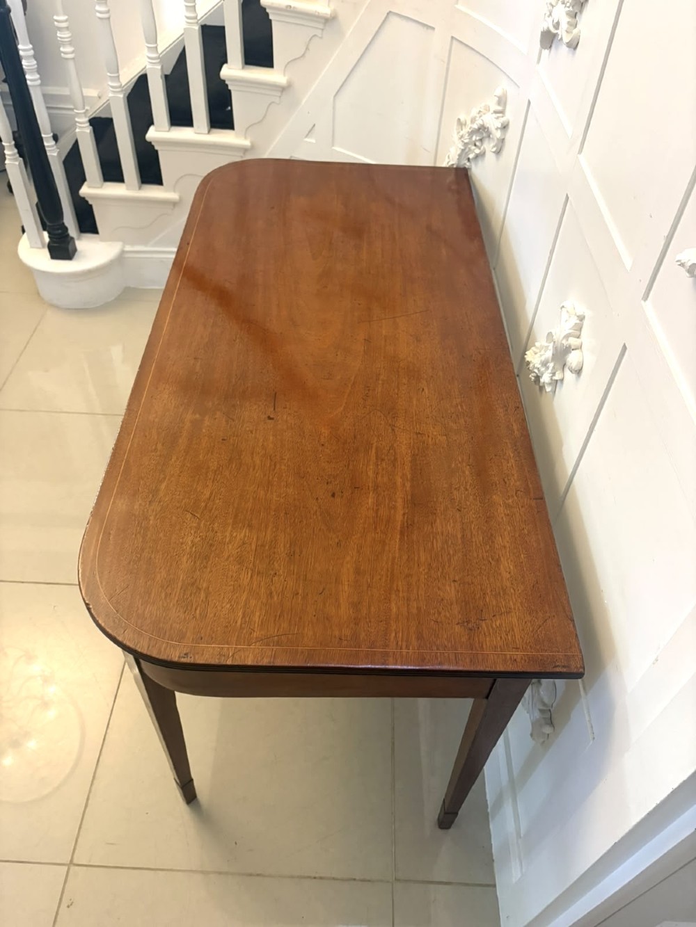 A pair of Georgian mahogany console tables featuring rounded corners, inlaid aprons, and slender tapered legs. View IX