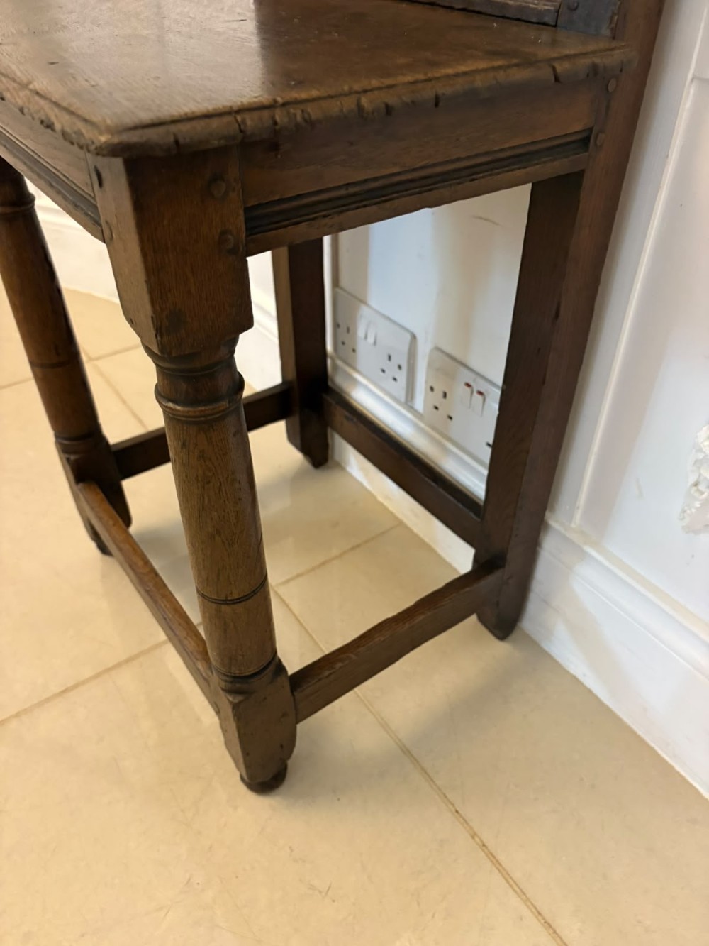 A dark oak 17th-century correction chair featuring a tall panelled backrest, carved crest rail with small wooden finials, solid wooden seat, turned front legs, and plain stretchers. View IV