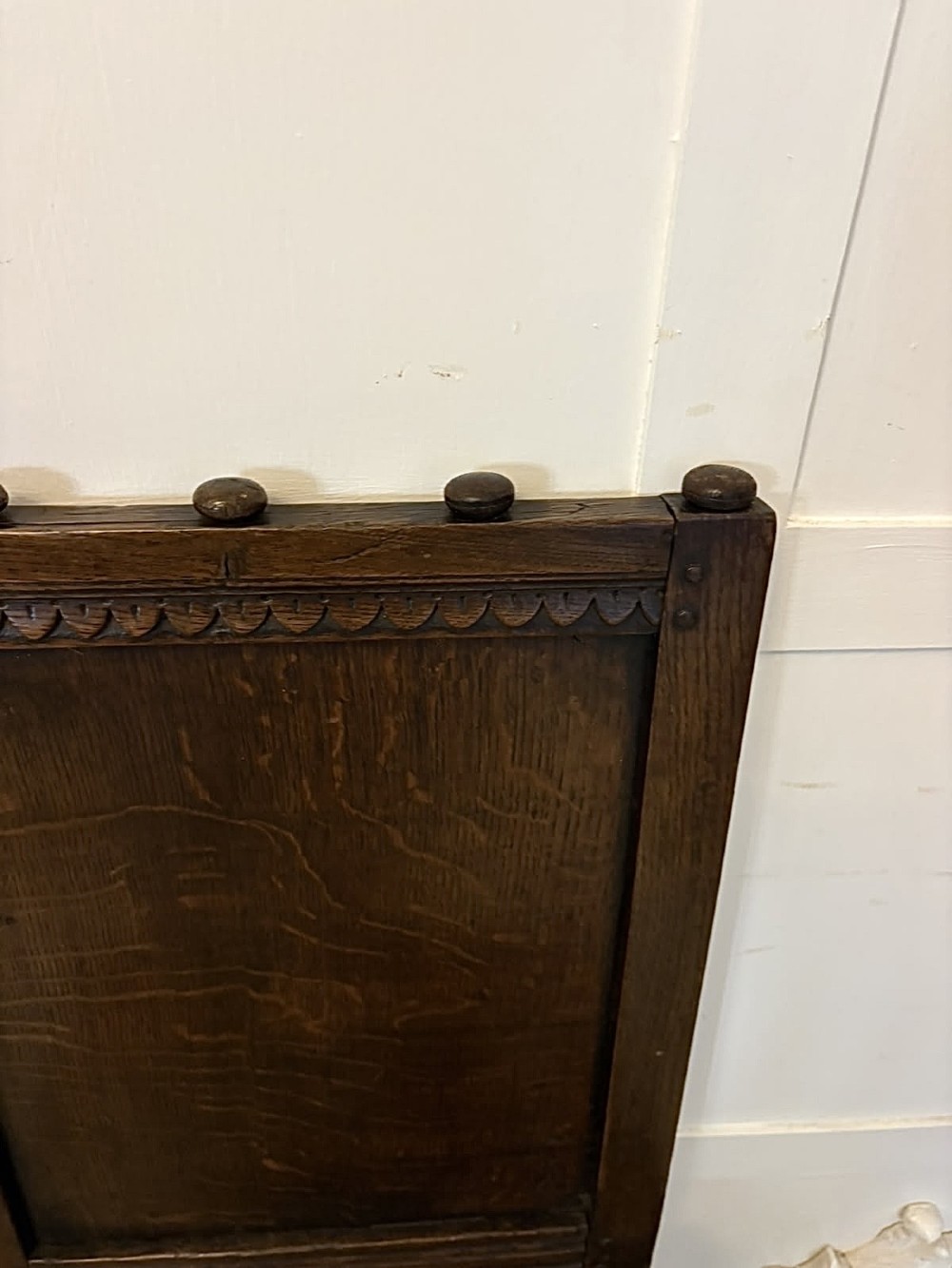 A dark oak 17th-century correction chair featuring a tall panelled backrest, carved crest rail with small wooden finials, solid wooden seat, turned front legs, and plain stretchers. View VIII