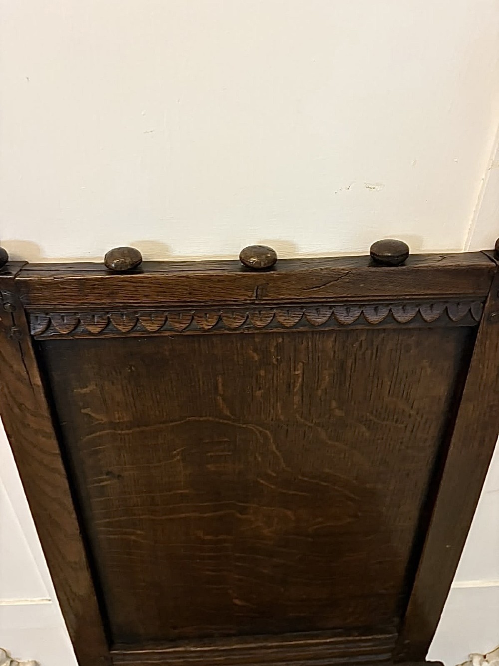 A dark oak 17th-century correction chair featuring a tall panelled backrest, carved crest rail with small wooden finials, solid wooden seat, turned front legs, and plain stretchers. View IX