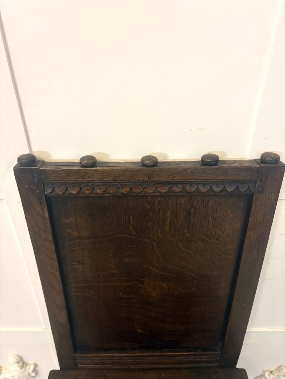 A dark oak 17th-century correction chair featuring a tall panelled backrest, carved crest rail with small wooden finials, solid wooden seat, turned front legs, and plain stretchers. View X