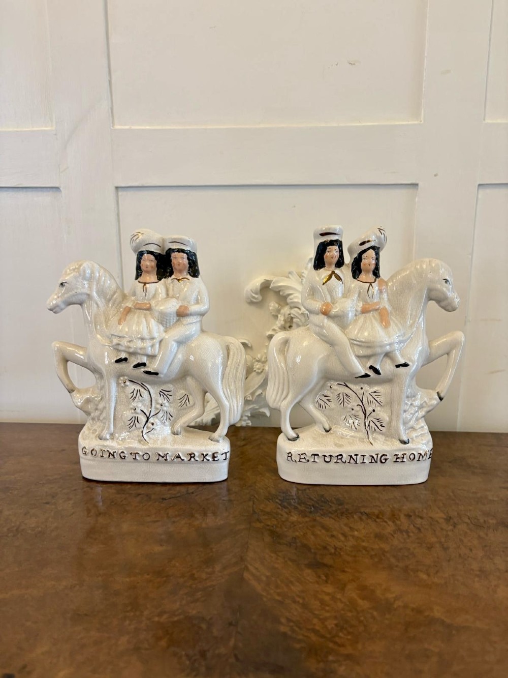 A pair of off-white antique Staffordshire flatback ceramic figures featuring riders on horseback titled Going to Market and Returning Home.