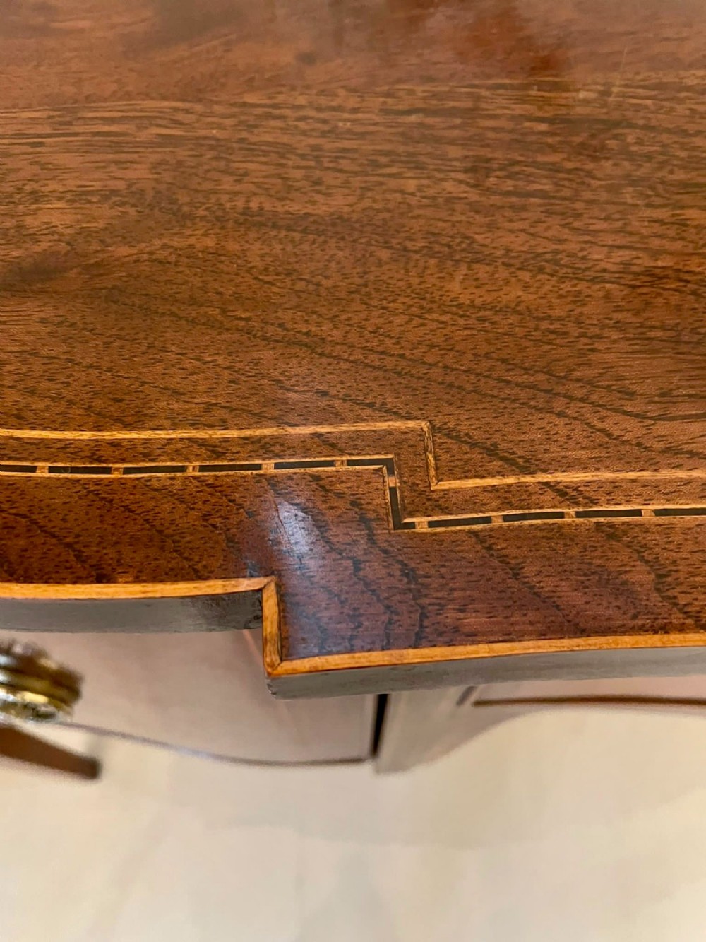 An Edwardian inlaid mahogany serpentine sideboard featuring a central drawer, flanking cupboard doors, brass circular handles, and tapered legs. View III