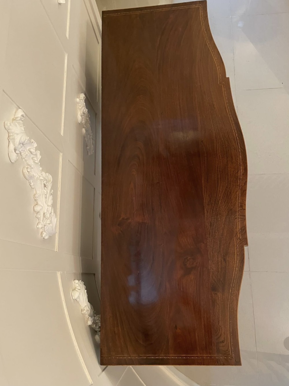 An Edwardian inlaid mahogany serpentine sideboard featuring a central drawer, flanking cupboard doors, brass circular handles, and tapered legs. View XI