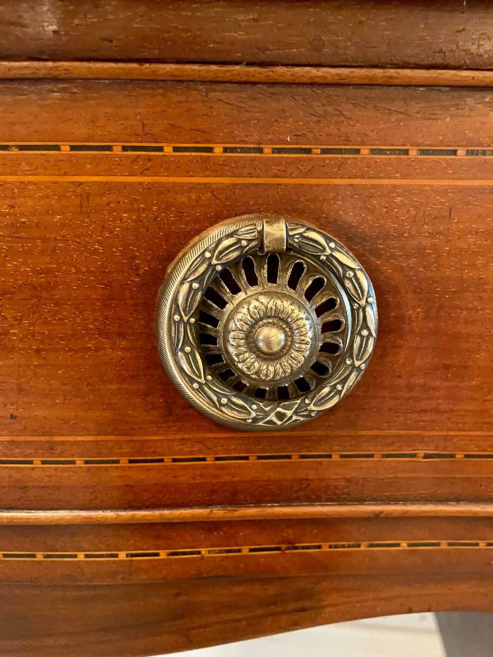 An Edwardian inlaid mahogany serpentine sideboard featuring a central drawer, flanking cupboard doors, brass circular handles, and tapered legs. View XII