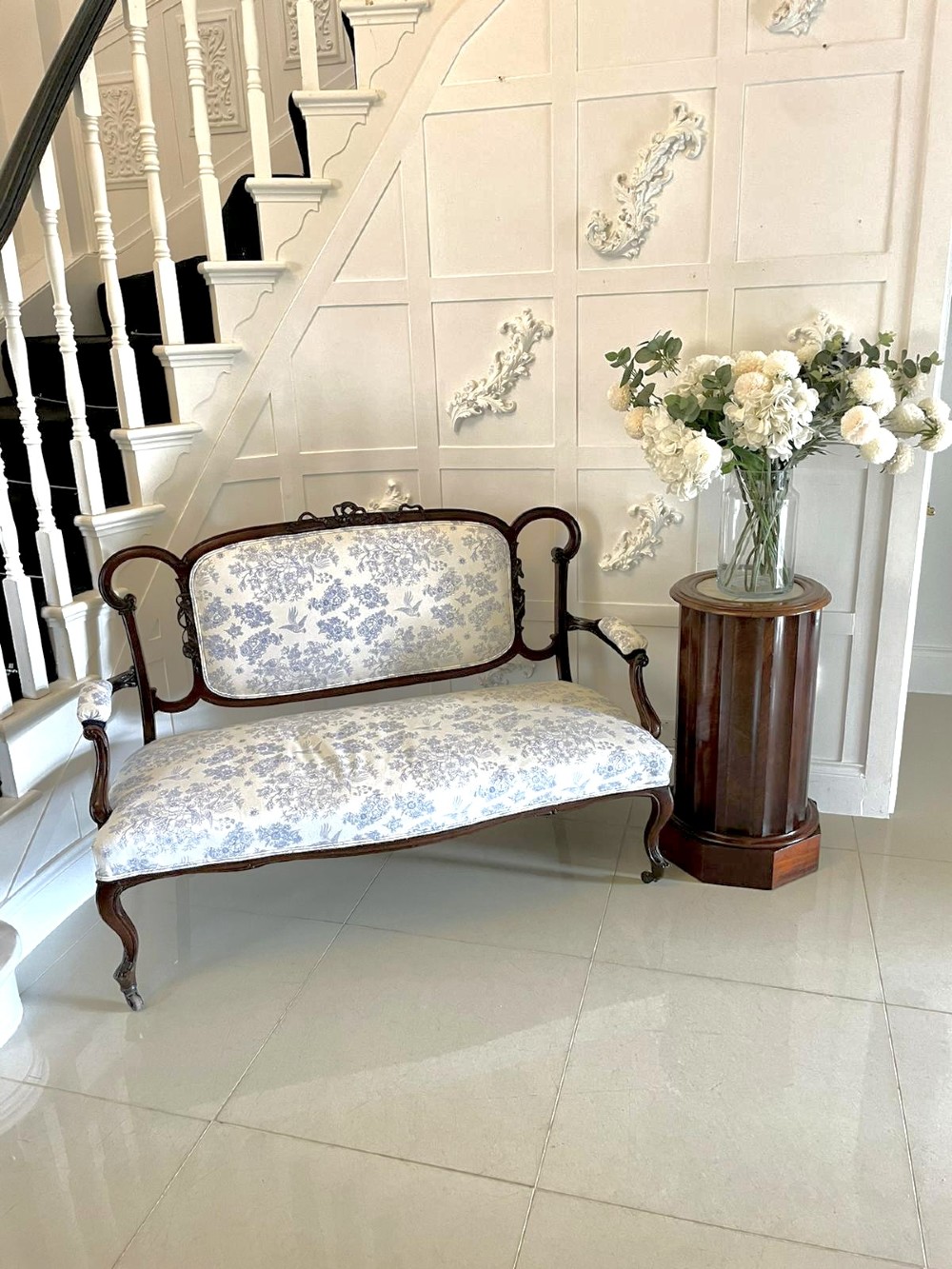 A Victorian carved mahogany settee featuring upholstered blue and white floral pattern seat and backrest, padded armrests, and carved cabriole legs. View II