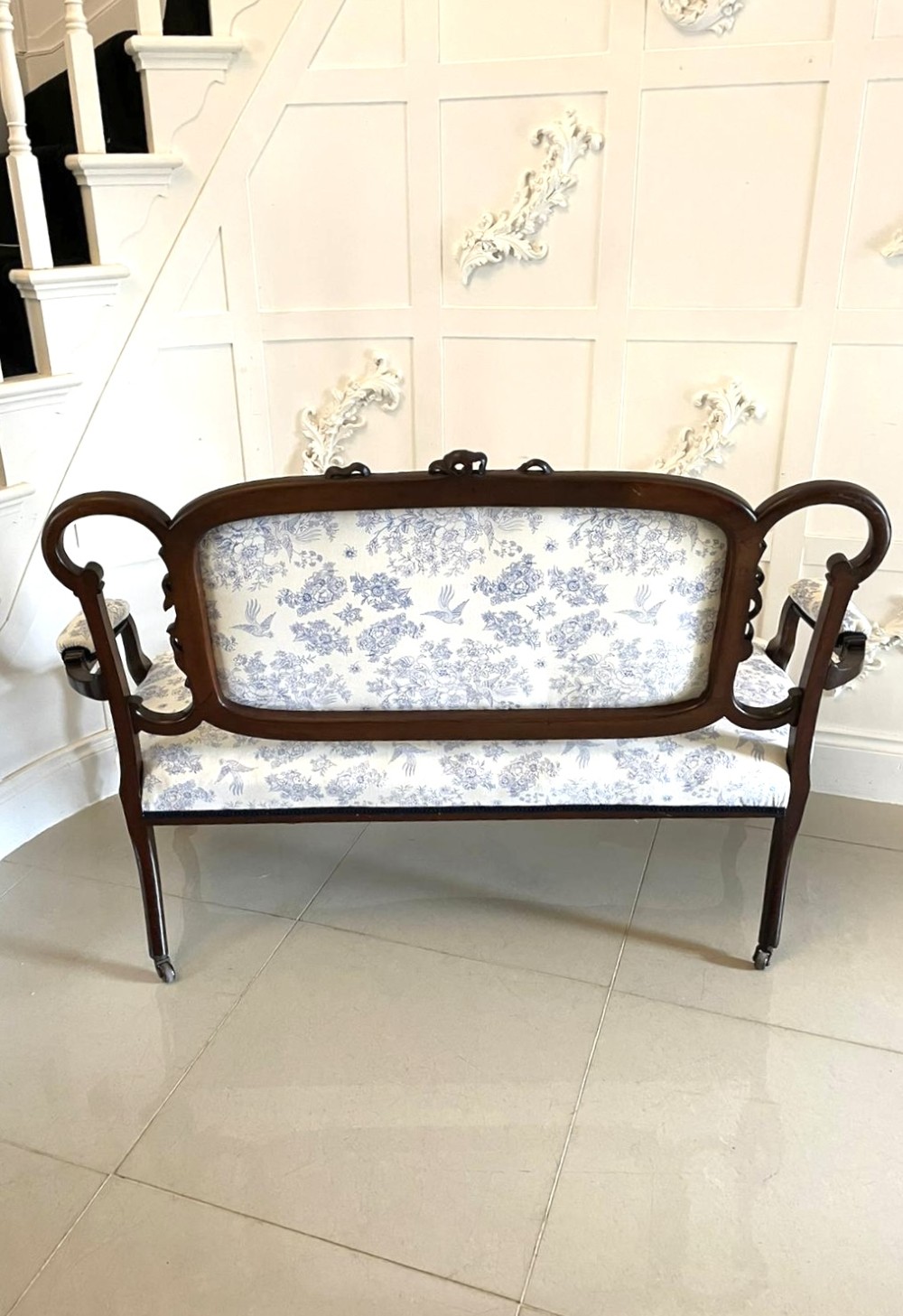 A Victorian carved mahogany settee featuring upholstered blue and white floral pattern seat and backrest, padded armrests, and carved cabriole legs. View V