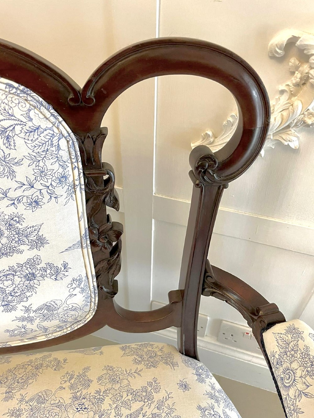 A Victorian carved mahogany settee featuring upholstered blue and white floral pattern seat and backrest, padded armrests, and carved cabriole legs. View X
