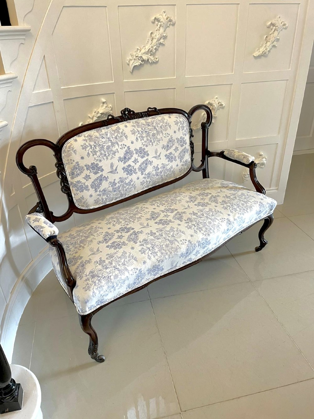A Victorian carved mahogany settee featuring upholstered blue and white floral pattern seat and backrest, padded armrests, and carved cabriole legs. View XII
