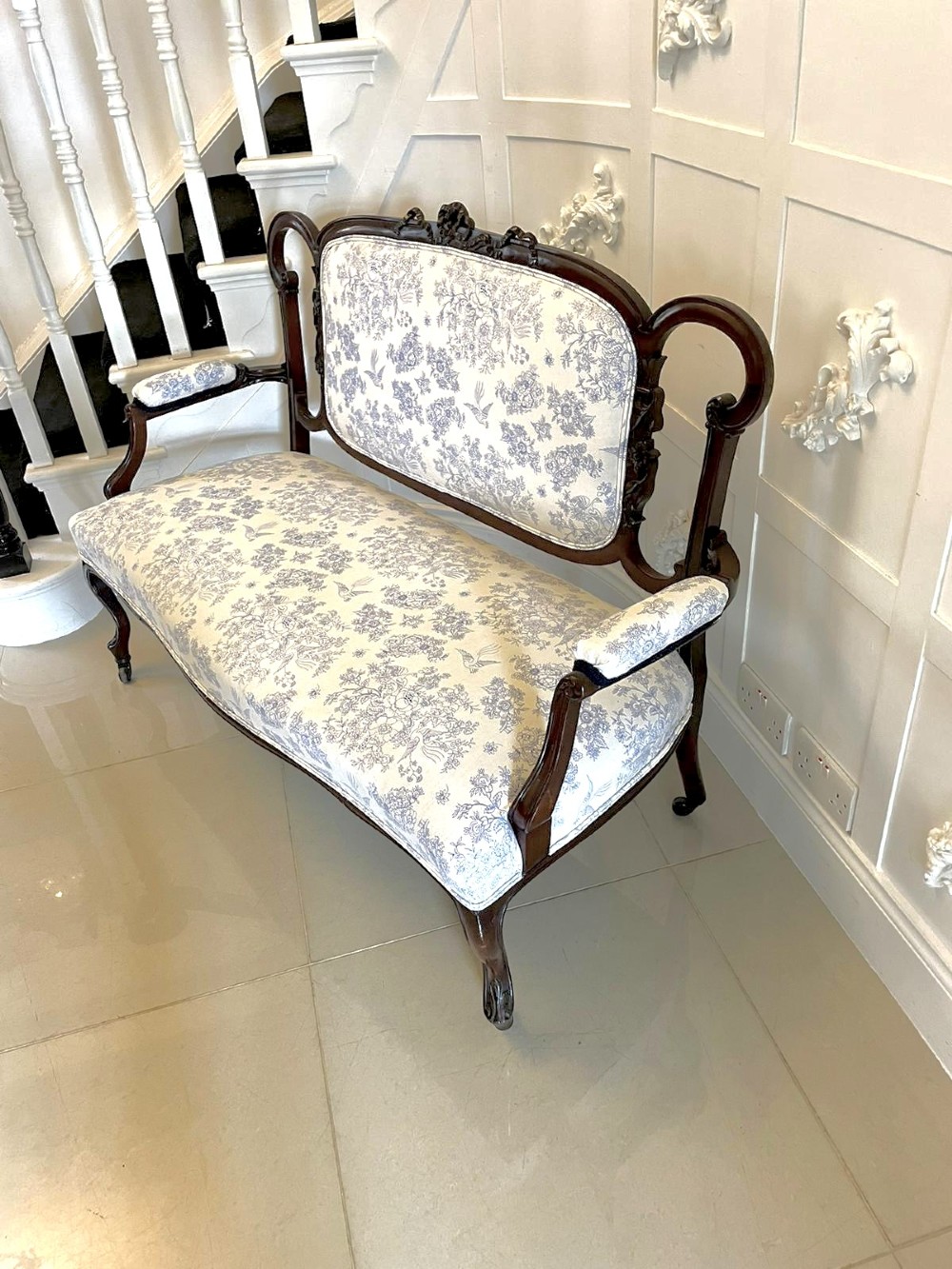 A Victorian carved mahogany settee featuring upholstered blue and white floral pattern seat and backrest, padded armrests, and carved cabriole legs. View XIII