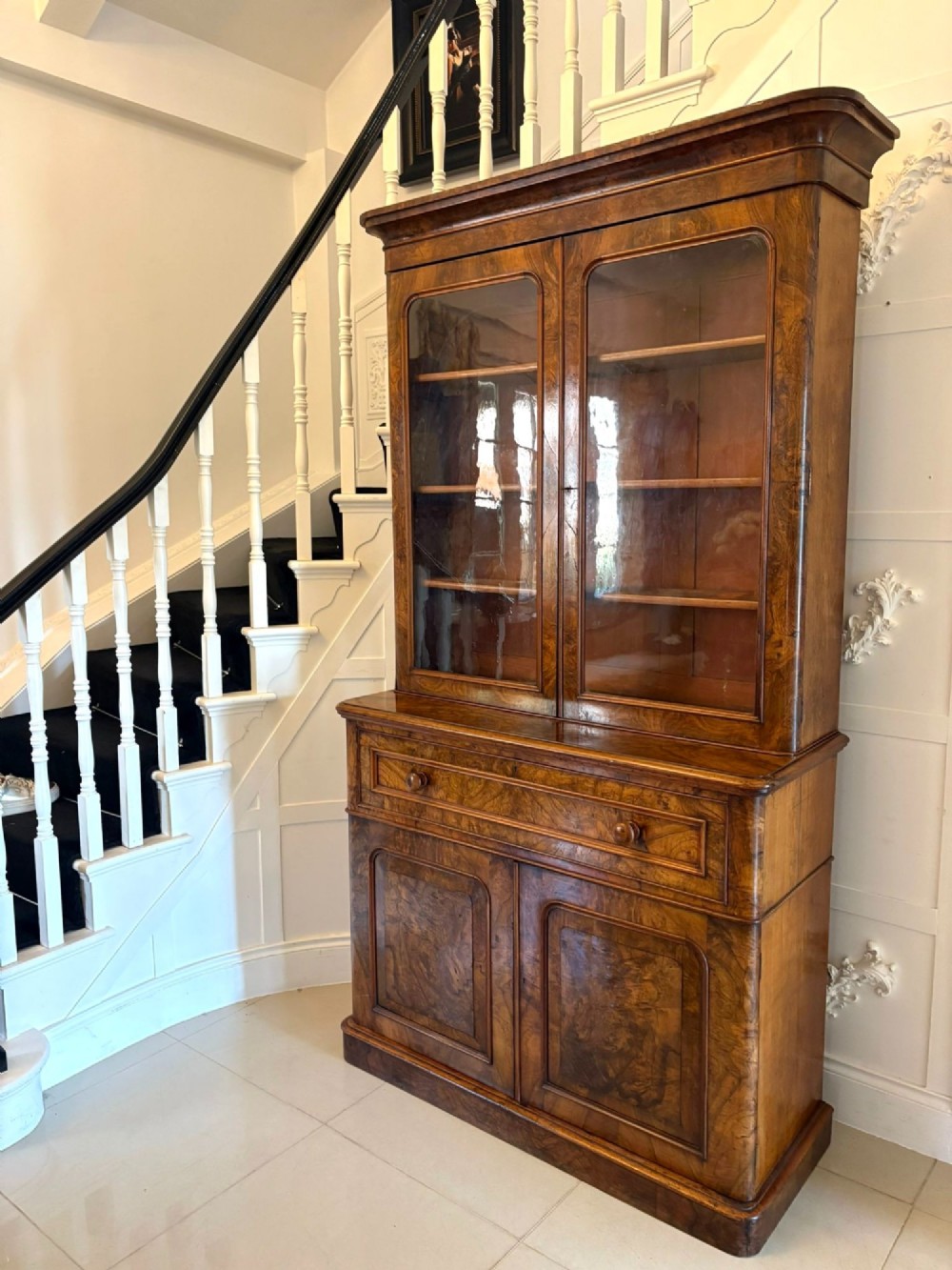 A Victorian burr walnut secretaire bookcase featuring a glazed upper cabinet with two doors, a deep secretaire drawer with turned wooden handles, and a two-door cupboard base. View V