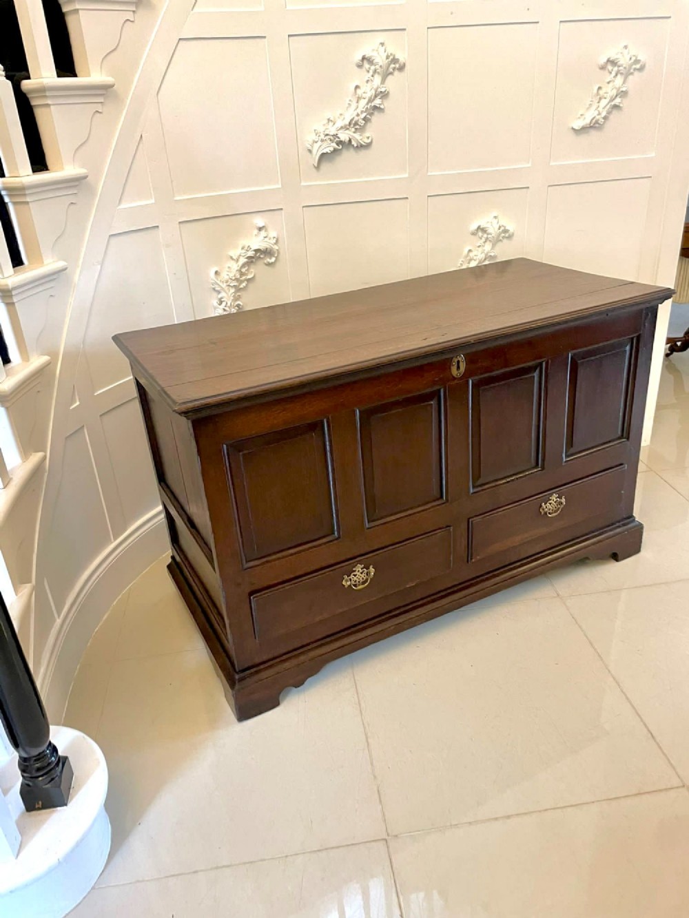 An 18th-century dark oak mule chest featuring four panelled facade sections above two lower drawers with brass handles.