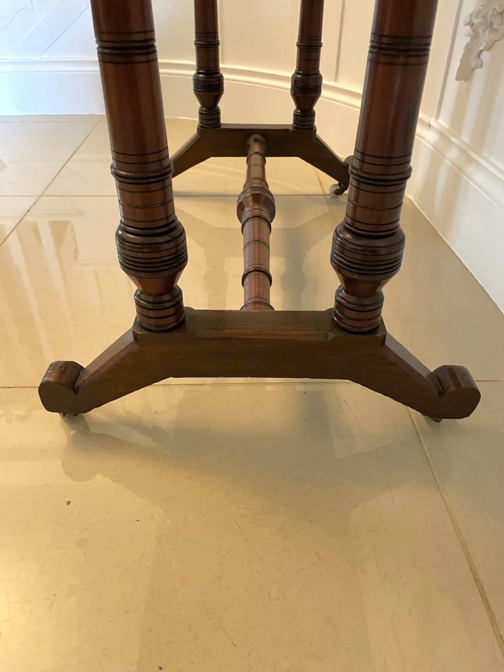 An Arts and Crafts oak side table featuring dark ebony inlay around the rectangular fold-over top, dual turned legs on a stretcher base, and ceramic castors. View V