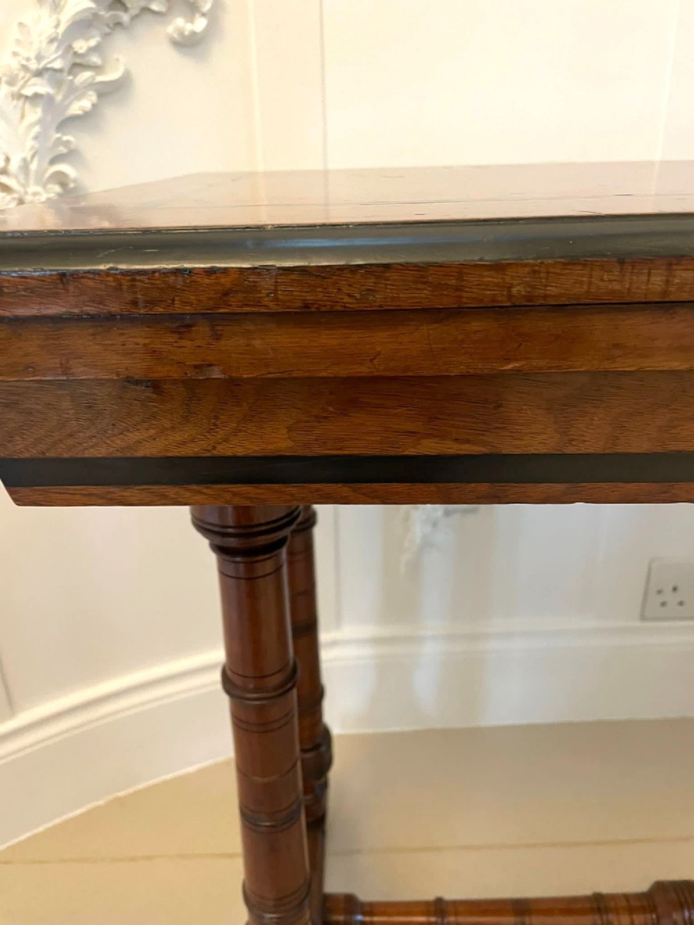 An Arts and Crafts oak side table featuring dark ebony inlay around the rectangular fold-over top, dual turned legs on a stretcher base, and ceramic castors. View VI