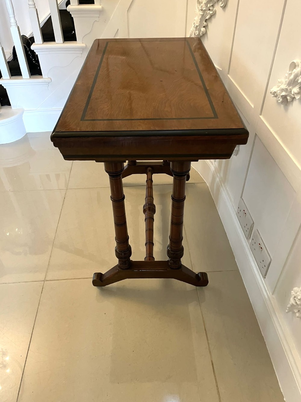 An Arts and Crafts oak side table featuring dark ebony inlay around the rectangular fold-over top, dual turned legs on a stretcher base, and ceramic castors. View VII