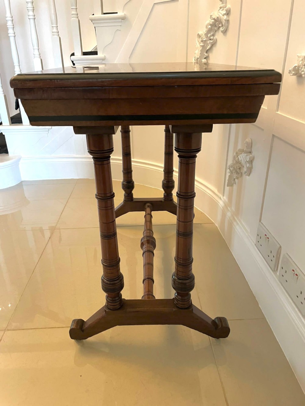 An Arts and Crafts oak side table featuring dark ebony inlay around the rectangular fold-over top, dual turned legs on a stretcher base, and ceramic castors. View XI