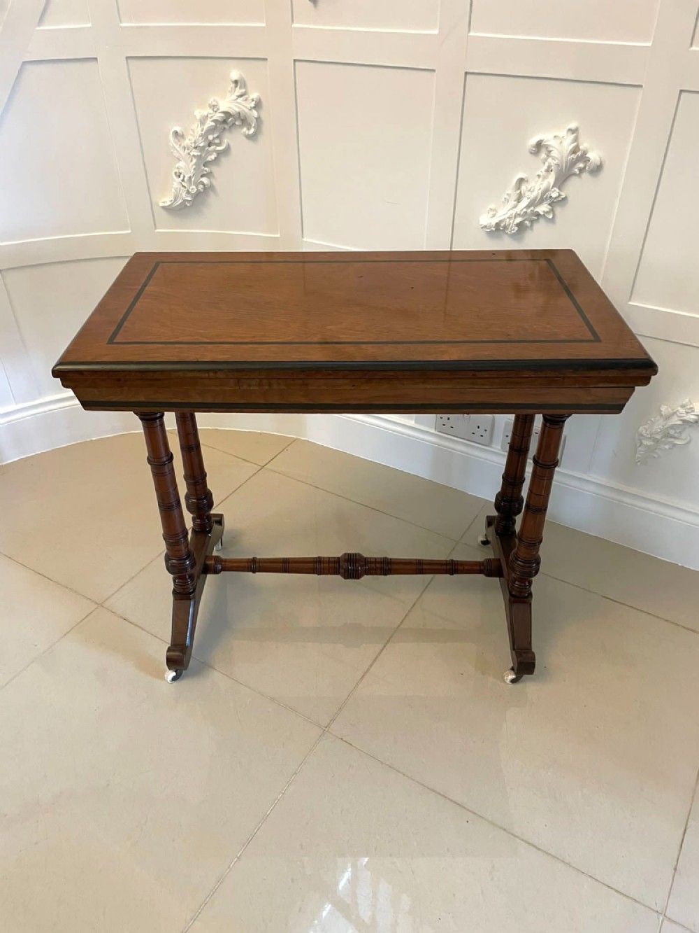 An Arts and Crafts oak side table featuring dark ebony inlay around the rectangular fold-over top, dual turned legs on a stretcher base, and ceramic castors. View XII