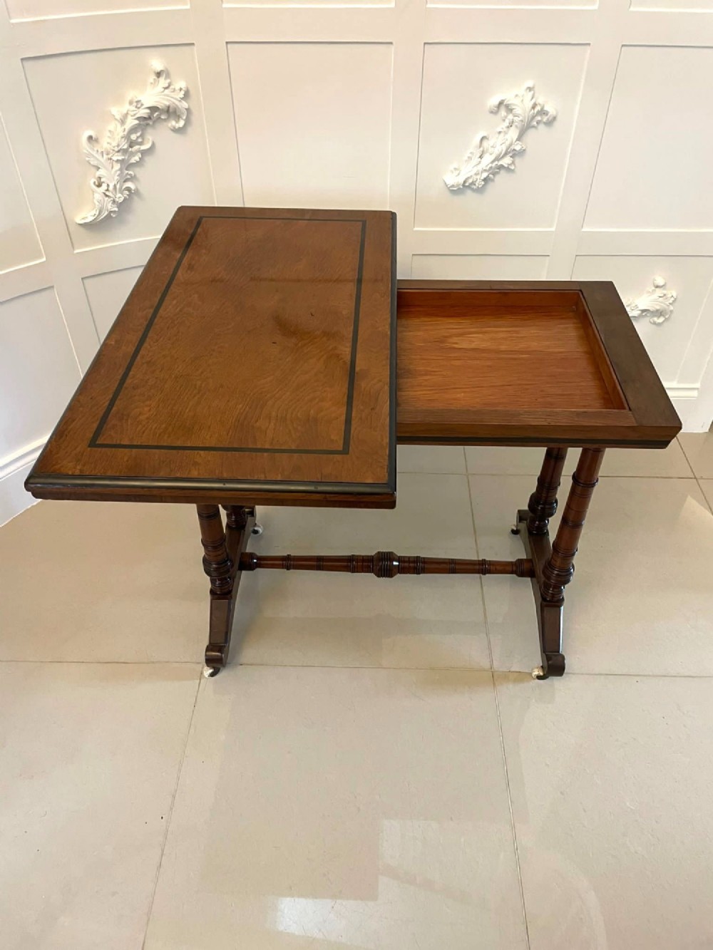 An Arts and Crafts oak side table featuring dark ebony inlay around the rectangular fold-over top, dual turned legs on a stretcher base, and ceramic castors. View XIII