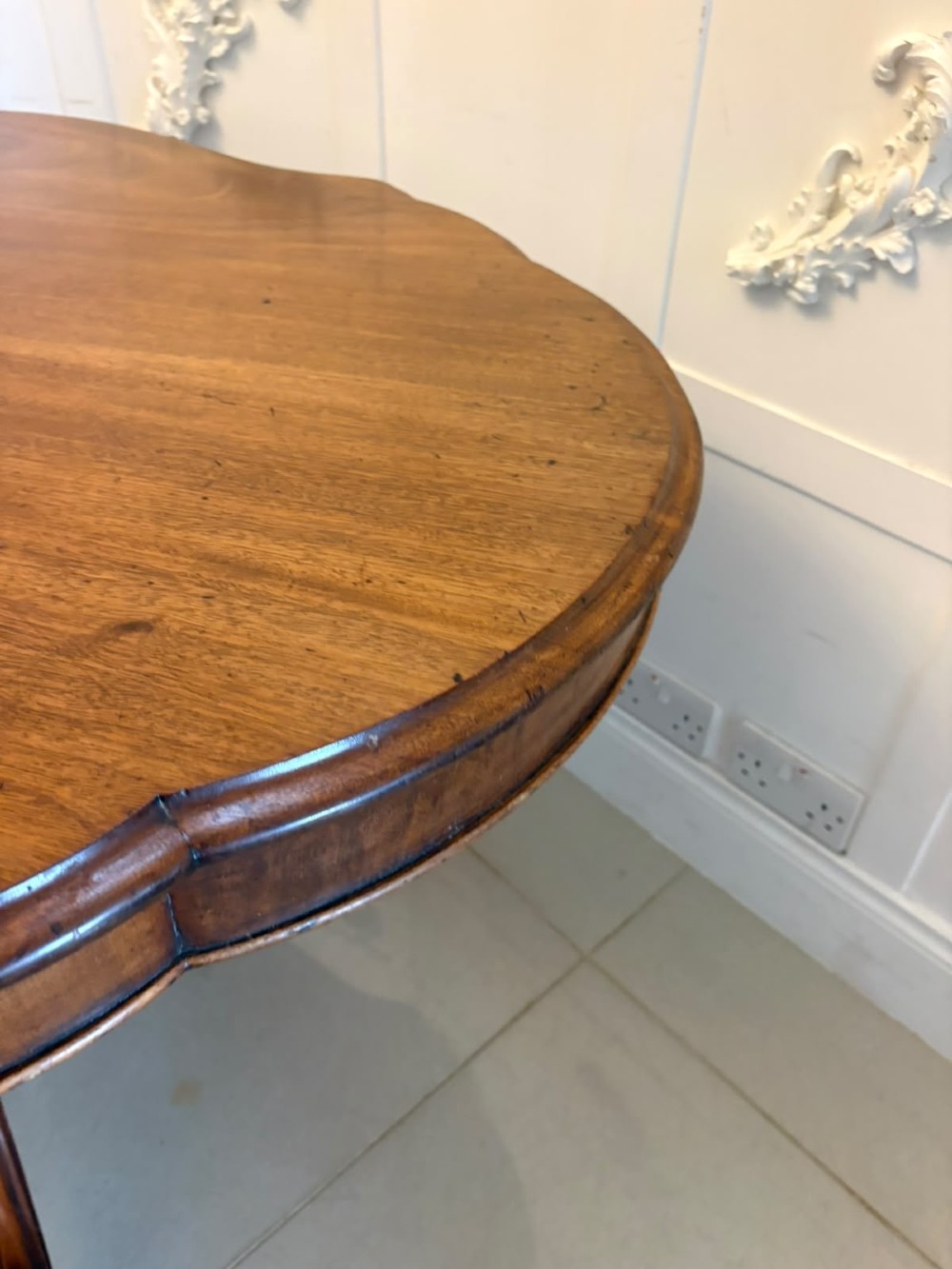 A Victorian figured mahogany tilt-top centre table featuring a shaped serpentine top positioned vertically on a carved central pedestal with four splayed legs. View V