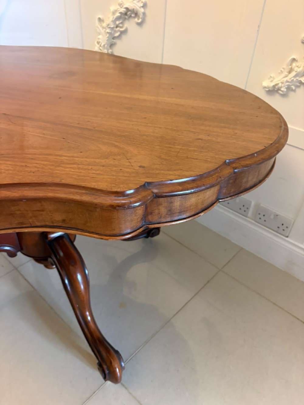 A Victorian figured mahogany tilt-top centre table featuring a shaped serpentine top positioned vertically on a carved central pedestal with four splayed legs. View VI